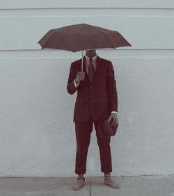Man under umbrella standing against concrete wall