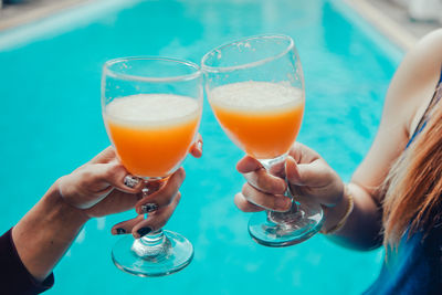 Cropped hands toasting drinks against swimming pool