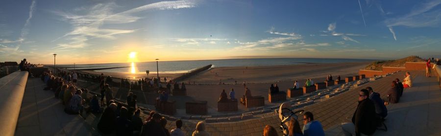 Panoramic view of people on beach against sky during sunset