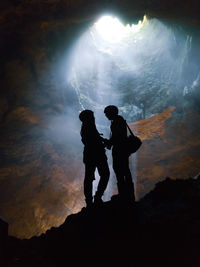 Silhouette man and woman standing on rock in cave