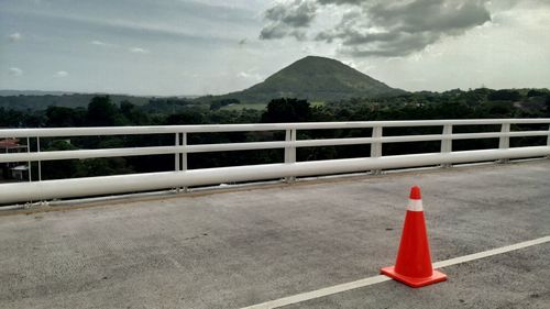 Road sign by railing on mountain against sky