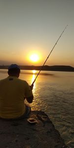 Rear view of man fishing in sea at sunset