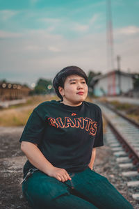 Portrait of man sitting on railroad track against sky