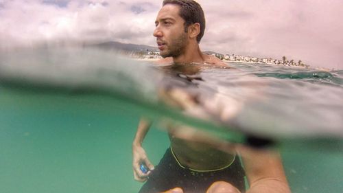 Man swimming at sea against cloudy sky