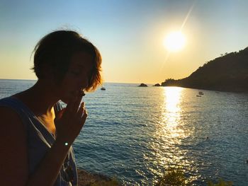 Young woman looking at sea against sky during sunset