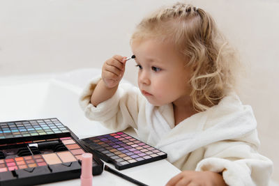 Toddler girl doing herself makeup with mama's cosmetics pretending grownup. applying eyeshadows