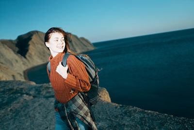 Woman standing on rock by sea against sky