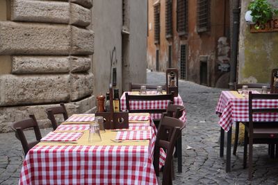 Empty chairs and tables at sidewalk cafe against building