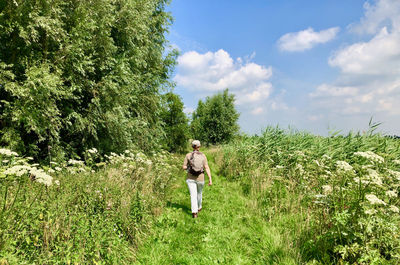 Rear view of woman walking on field against sky