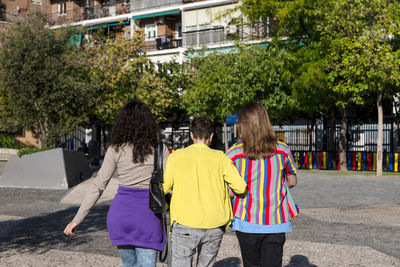 Young friends embracing while walking outdoors with the lgbt rainbow flag.