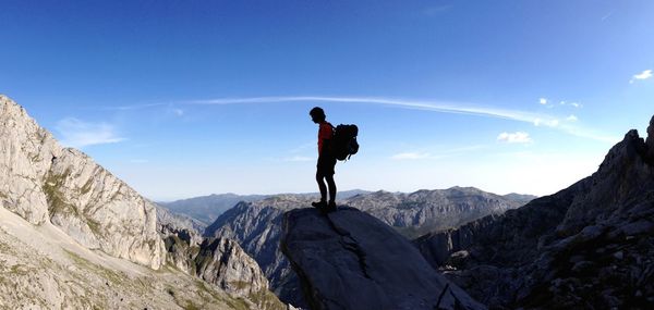 Side view of male hiker standing on mountain against blue sky