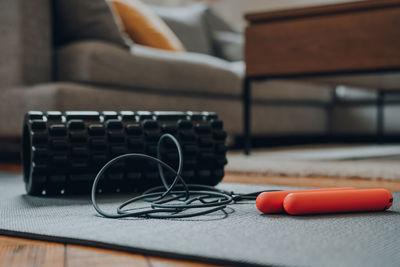 Close up of a jump rope and a foam roller on a fitness mat, modern interior, selective focus.