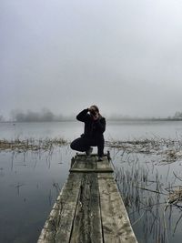 Rear view of woman standing on pier against lake