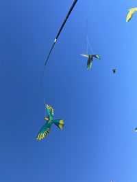 Low angle view of kites flying against clear blue sky