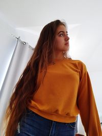 Young woman looking away while standing against wall