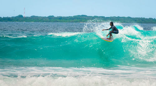 Young man surfing on sea against clear sky