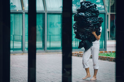 Man carrying garbage bags while walking on footpath seen through gate