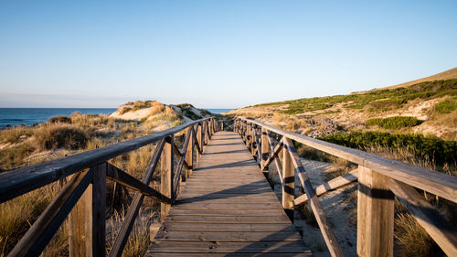 Wooden footbridge leading towards sea against clear sky