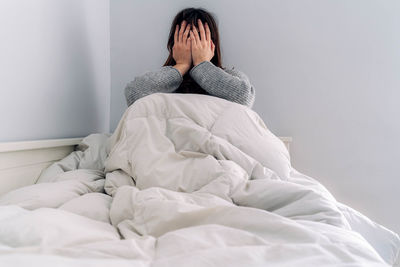 Full length of woman sitting on bed against wall