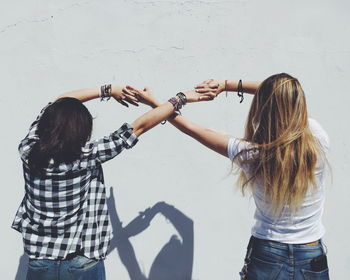 Rear view of female friends holding hands against wall