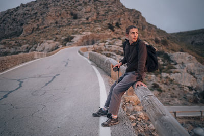 Young man looking away while sitting on railing with skateboard at sunset