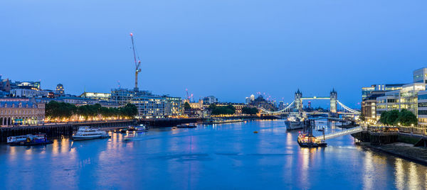 Illuminated bridge over river in city against clear blue sky