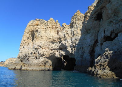 Rock formations in sea against clear blue sky