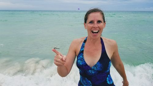 Portrait of smiling woman with dragonfly on index finger standing at beach