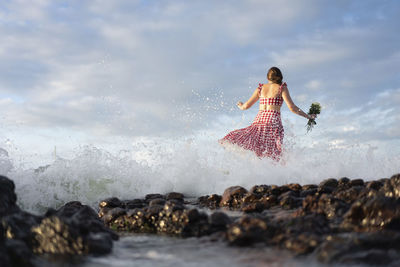 Woman on rock in sea against sky