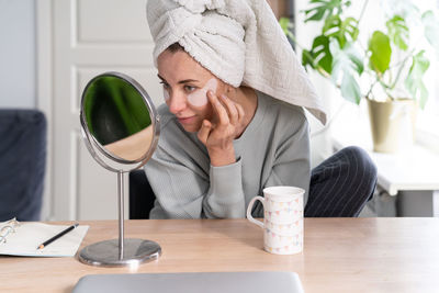 Woman applying eye patches by mirror on table