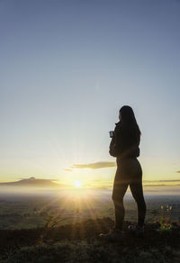 Rear view of woman standing against sky during sunset