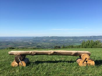 Wooden seat on grassy landscape against clear blue sky