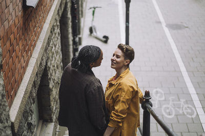 Smiling mid adult woman talking with girlfriend while standing by railing