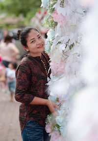Portrait of a smiling young woman standing by flowering plants