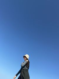 Low angle view of woman wearing sunglasses against clear blue sky