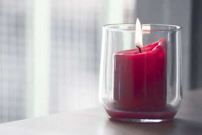 Burning red candle inside a clear glass vase. no people