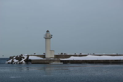 Lighthouse by sea against clear sky