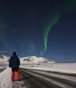 Rear view of man standing on road against sky at night