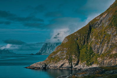 Scenic view of sea by mountain against sky