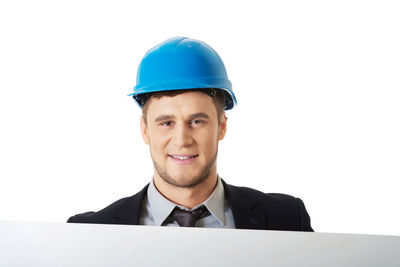 Close-up portrait of businessman wearing blue hardhat while standing against white background