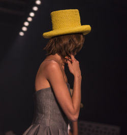 Side view of young woman wearing yellow hat at night