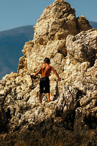 Full length of shirtless boy on rock in sea