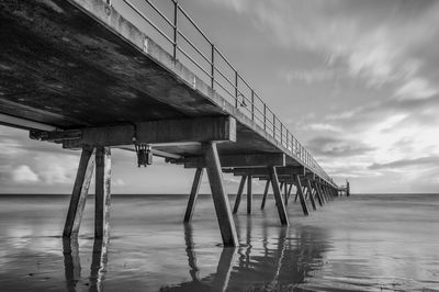 Low angle view of pier over sea against cloudy sky