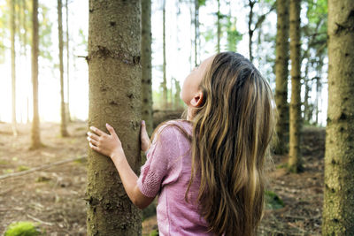 Girl holding tree trunk and looking up