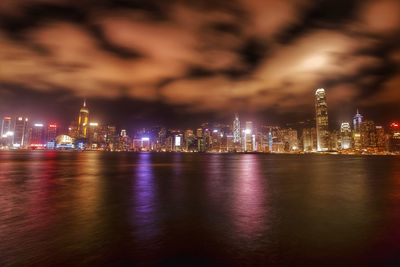 Illuminated city by sea against sky at night