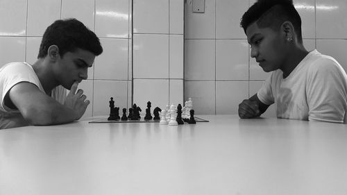 Side view of teenage boys playing chess at table