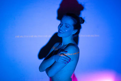 Young woman looking away while standing against blue sky