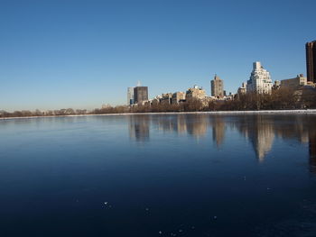 Scenic view of lake by buildings against clear blue sky