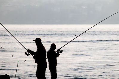 Silhouette man fishing at sea against sky