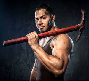 Portrait of muscular man holding pick axe against wall